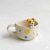 Polka-dot ceramic mug with a smiling miniature dog figurine peeking over the rim.